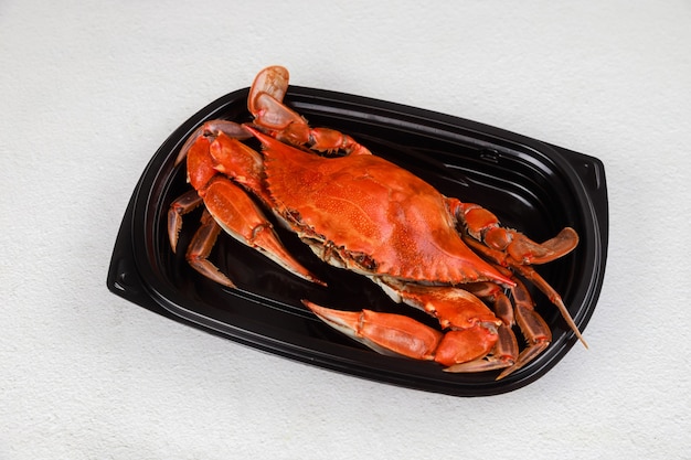 Cooked crab on black plastic plate on white background.