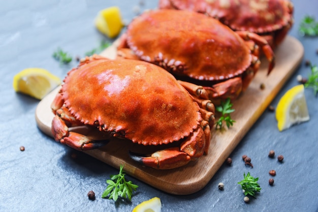 Cooked crabs on wooden board with lemon on plate served on dark plate top view - stone crab steamed seafood 