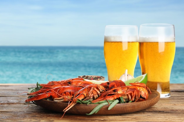 Cooked crayfishes served with beer on wooden table near sea