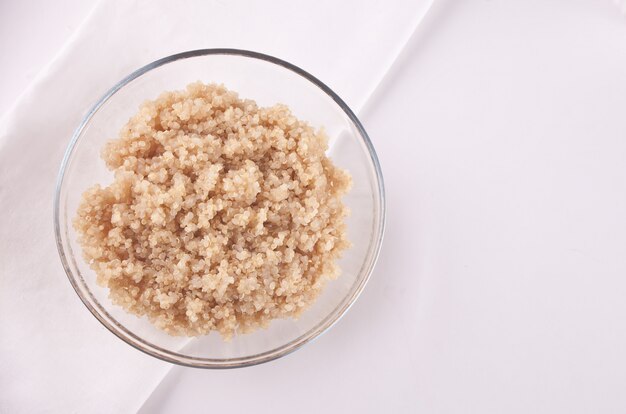 Quinoa deliziosa cucinata in ciotola di vetro con tovagliolo bianco sul tavolo bianco.