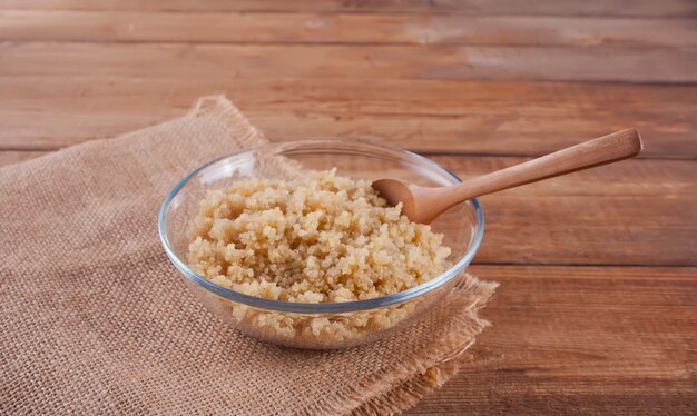 Cooked delicious quinoa in glass bowl with wooden spoon on the wooden table