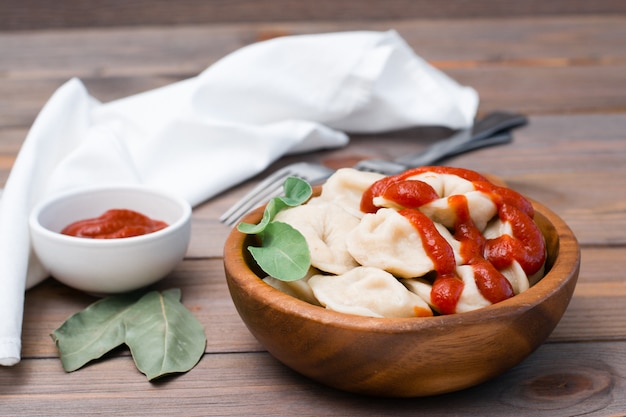 Photo cooked dumplings poured with ketchup with arugula leaves in a wooden bowl on a table