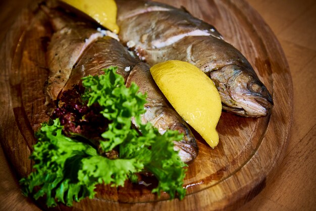 Приготовленная рыба с лимоном и салат на деревянной доске.