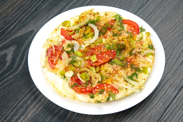 Cooked fried omelet with herbs and vegetables in a white plate on a wooden table