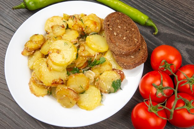 Cooked fried potatoes with herbs and vegetables in a white plate on a wooden table