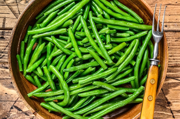 Cooked green beans in a wooden plate. wooden table. top view.