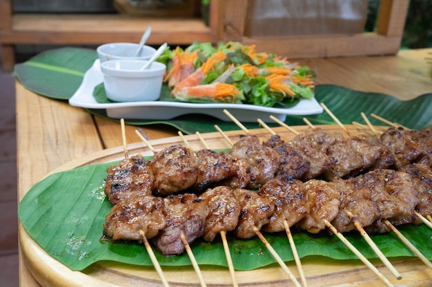 Cooked grilled roasted pork sticks are arranged on the banana leaf  at outside garden