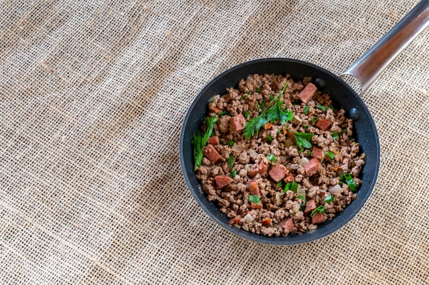 Cooked ground beef with bacon and parsley spices in the skillet top view Cooked ground beef