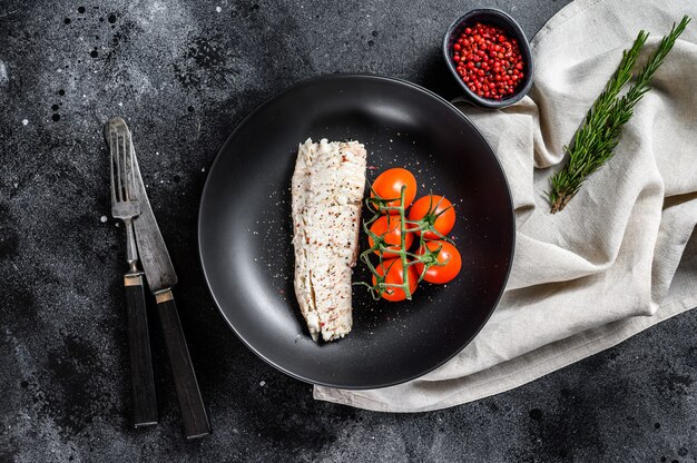 Cooked haddock fillet with cherry tomatoes. Black background. Top view