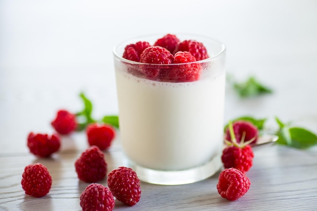 Cooked homemade yogurt with ripe red raspberries in a glass on a wooden table