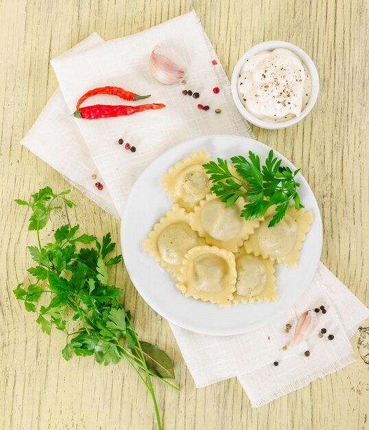 Cooked italian ravioli in white plate on rustic wooden background