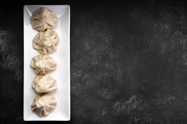 Cooked khinkali on a white plate on a dark background