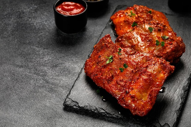 Cooked marinated pork bbq ribs baked ribs in marinade sauce on
board and dark background copy space