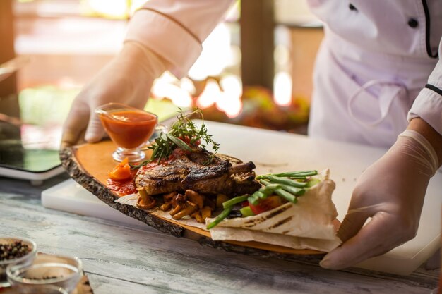 Cooked meat and pita bread. Hands hold board with food. Tasty dish with grilled pork. High calorie lunch in cafe.