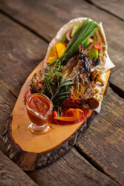 Cooked meat on wooden board. Herbs and bowl with sauce. Rustic recipe of grilled pork. Take a small bite.