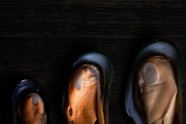 Cooked mussels of different sizes on a wooden background