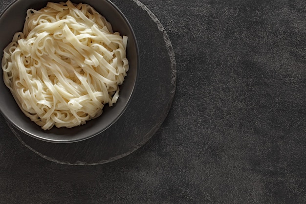 Cooked noodles on gray bowl on slate stone plate round dark background top view