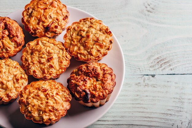 Cooked oatmeal muffins on white plate over light wooden background