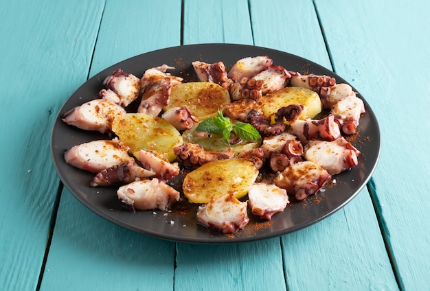 Cooked octopus presented sliced with potatoes, blue wood table