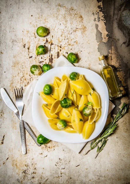 Cooked pasta with Brussels sprouts in a white plate with olive oil.  On rustic background.  Top view