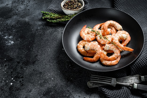 Cooked peeled king prawns, shrimps on a plate. Black background.