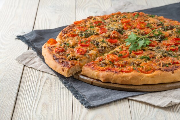 Cooked pizza on a wooden background with cut slice