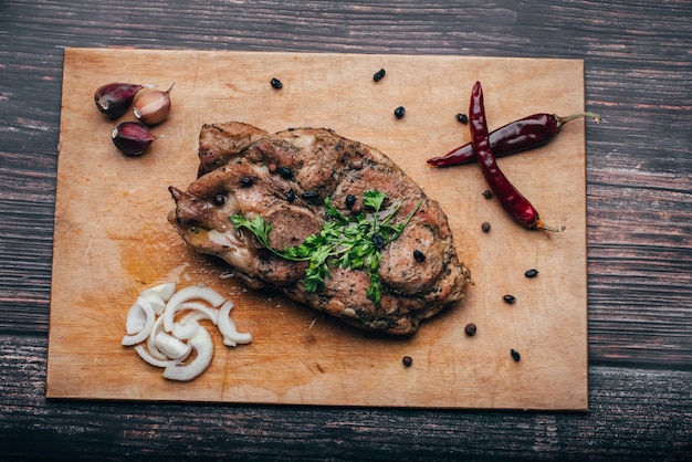 Приготовленное свиное мясо на деревянной доске с чесноком, луком, перцем