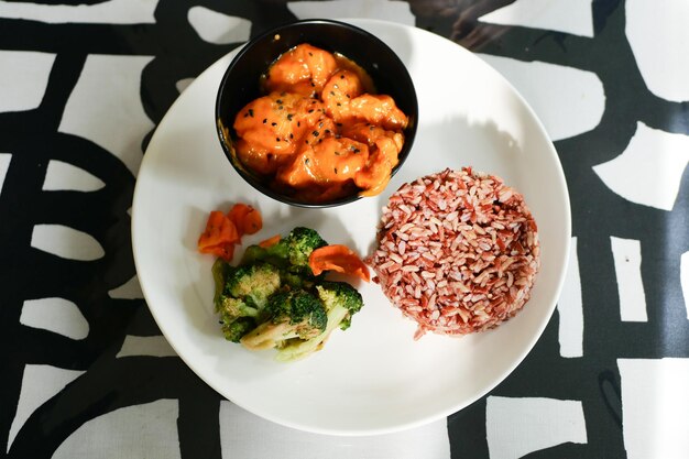 Cooked red rice vegetable salad and fish curry in a bowl on table