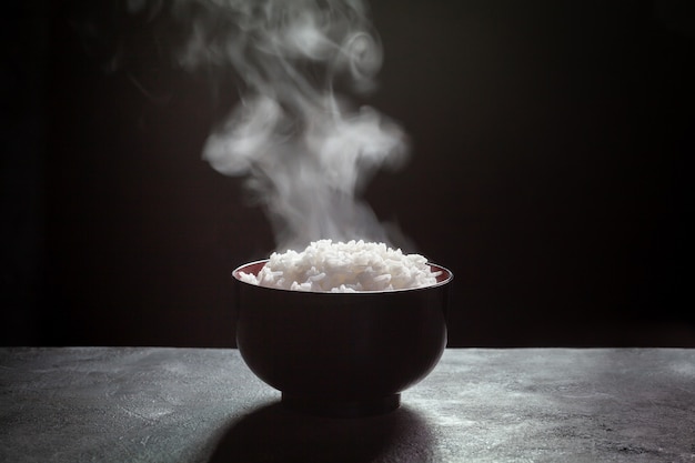 Photo cooked rice with steam in black bowl on dark