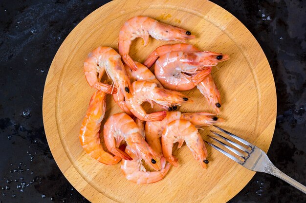 Cooked shrimps and fork on a wooden board