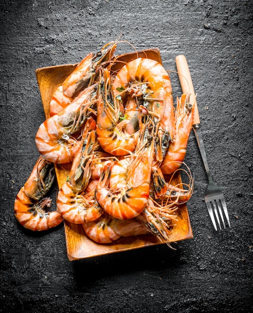 Photo cooked shrimps on a wooden plate with a fork