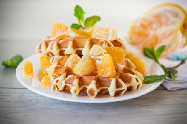 Cooked sweet Belgian waffles with oranges on the table