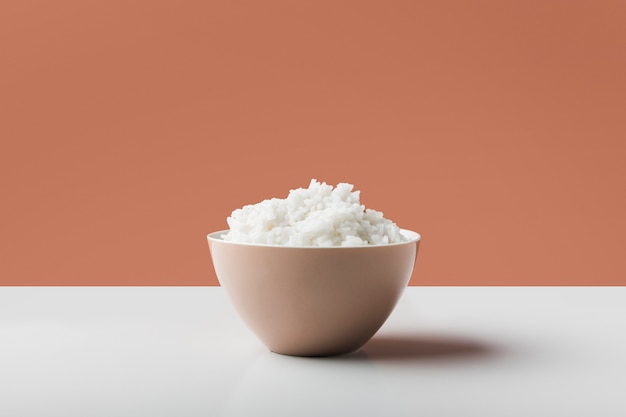 Cooked white boiled rice in the bowl on white table against brown background