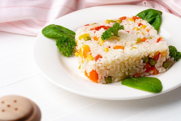 Cooked white rice mixed with colorful vegetables on white plate