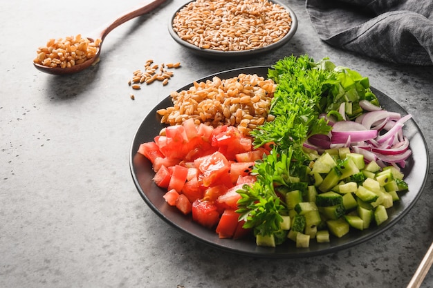 Cooked whole grain cereal spelt salad with seasonal vegetables in bowl on black background.