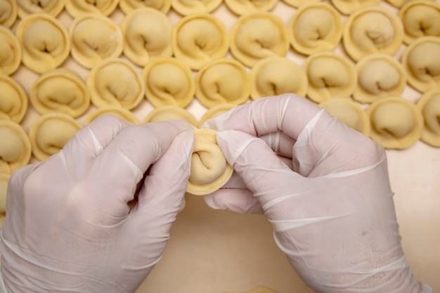 Cooker hands holding pelmeni with minced meat, top view