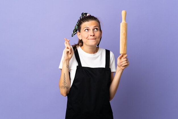 Cooker Slovak woman isolated on purple wall with fingers crossing and wishing the best