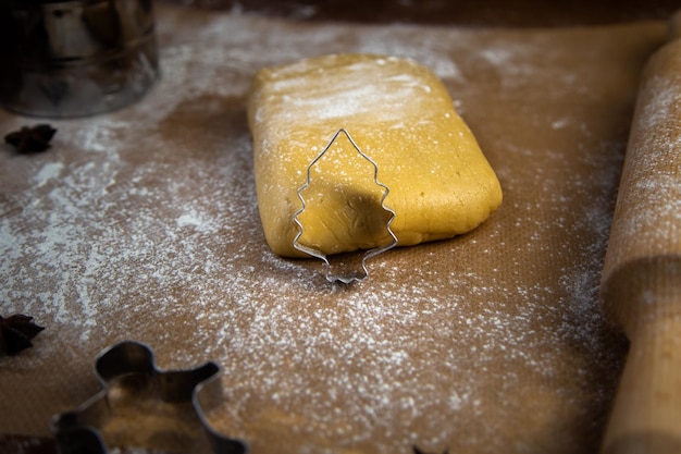 A cookie cutter in the form of a christmas tree leaned on the dough flour other cookie cutters and a...