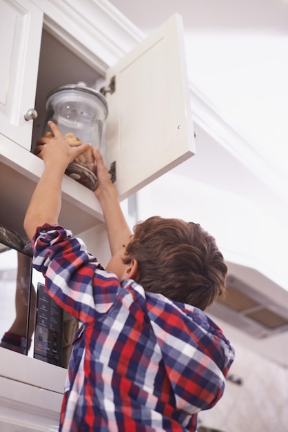 Cookie time A young boy reaching for a cookie jar in the top kitchen cupboard