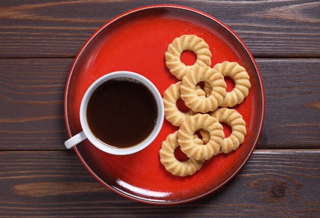 Cookies and coffee on a red plate on wooden table, top view