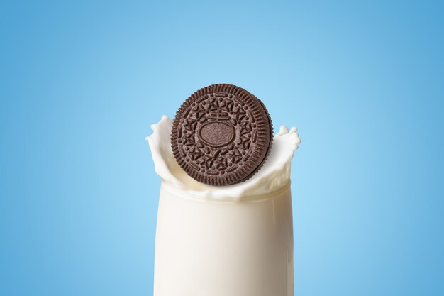 Cookies and cream of chocolate flavour dropped in fresh milk splash on blue background