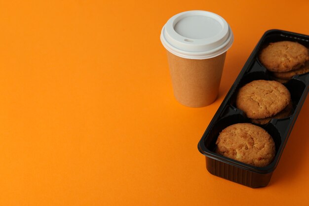 Cookies en papieren kopje koffie op oranje achtergrond.