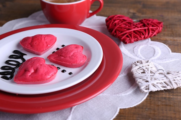 Cookies in form of heart in plate with cup of coffee on napkin, on rustic wooden planks background