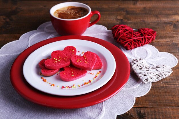 Cookies in form of heart in plate with cup of coffee on napkin, on rustic wooden planks background