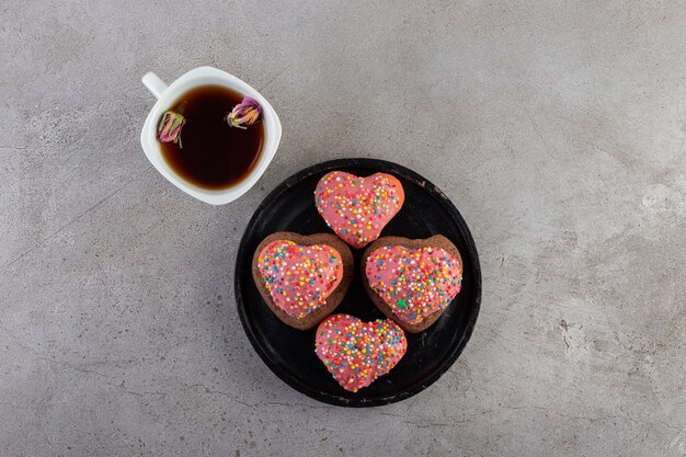 Cookies in heart shaped with sprinkles and a cup of tea placed on a stone table .