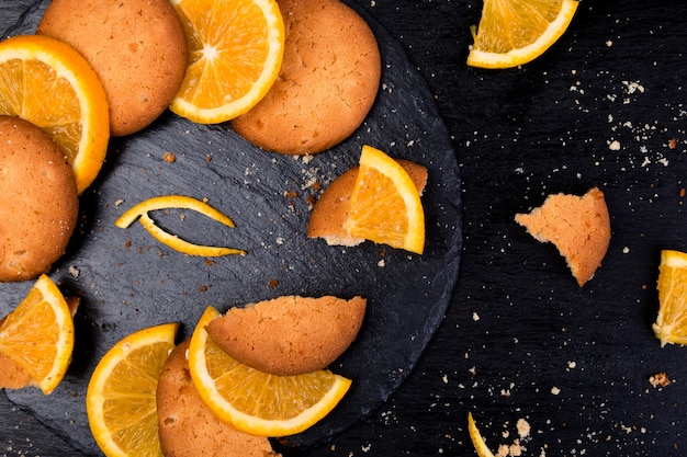 Cookies and orange citrus fruit on slate plate on black . Flat lay