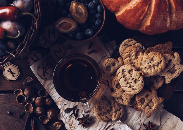 Печенье в виде тыквы и привидений в тарелке на столе Рядом с чайником и кружками осенний натюрморт