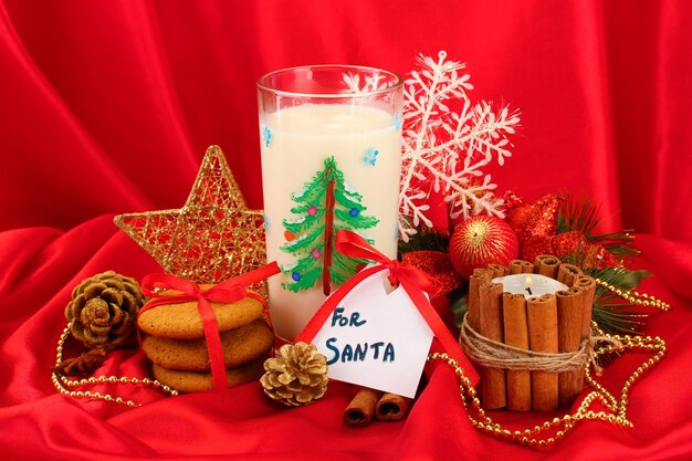 Cookies voor de kerstman: conceptueel beeld van gemberkoekjes, melk en kerstversiering op rode achtergrond