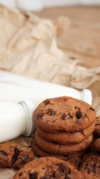 Biscotti con gocce di cioccolato su carta artigianale e bottiglie di latte. serpenti organici naturali fatti a mano per una sana colazione. foto verticale