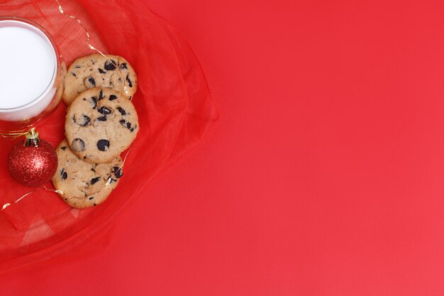 Cookies with chocolate with a glass of milk and a Christmas tree toy on a red Christmas background